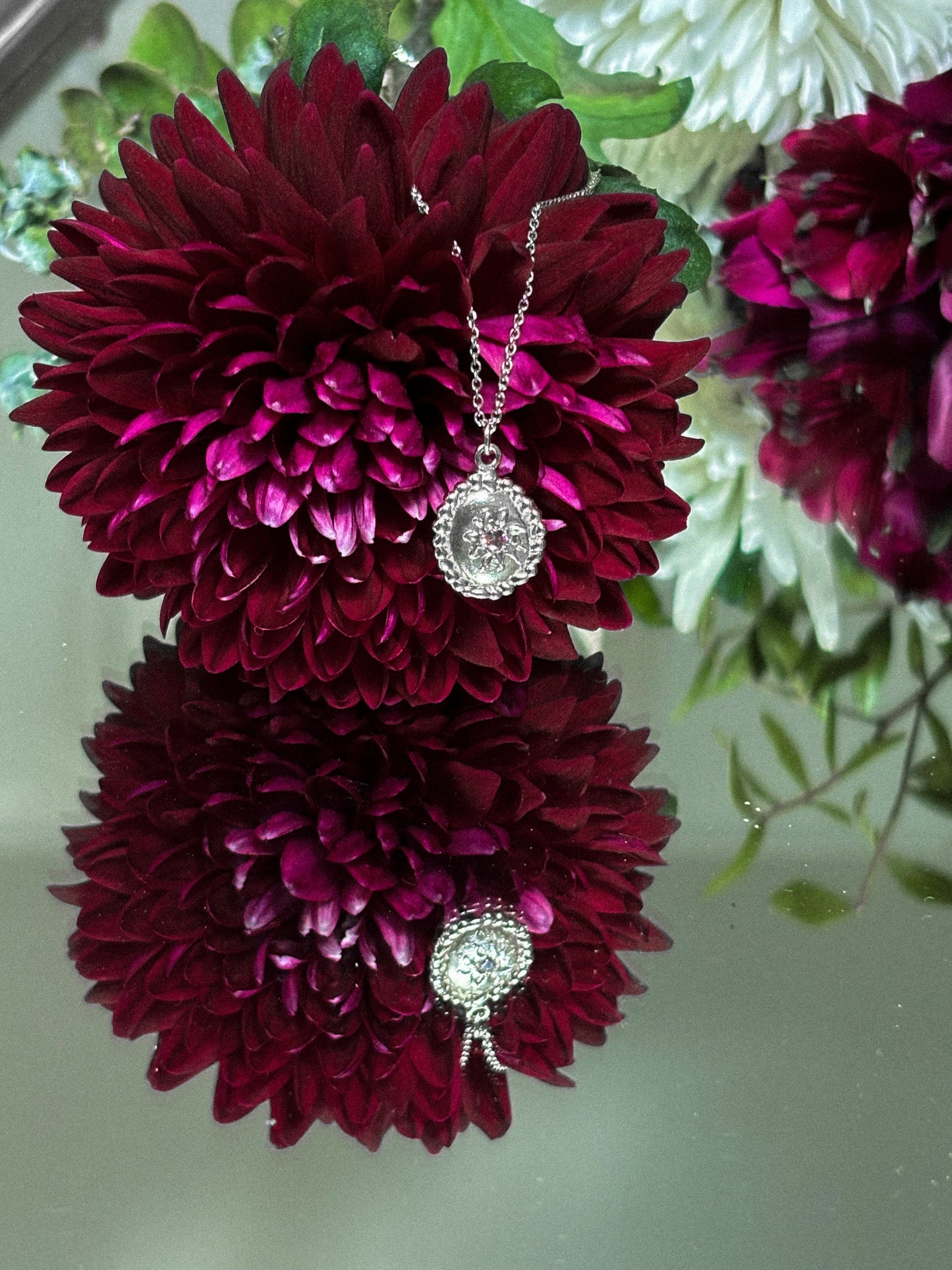 Necklace with a pendant displayed on maroon flowers against a light background