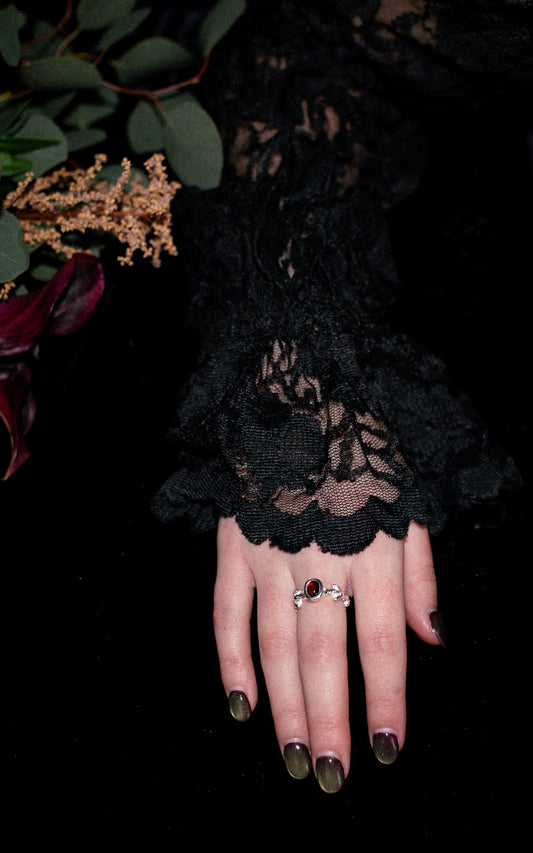 Hand wearing a black lace long sleeve with a silver ring with red oval gemstone on a dark background