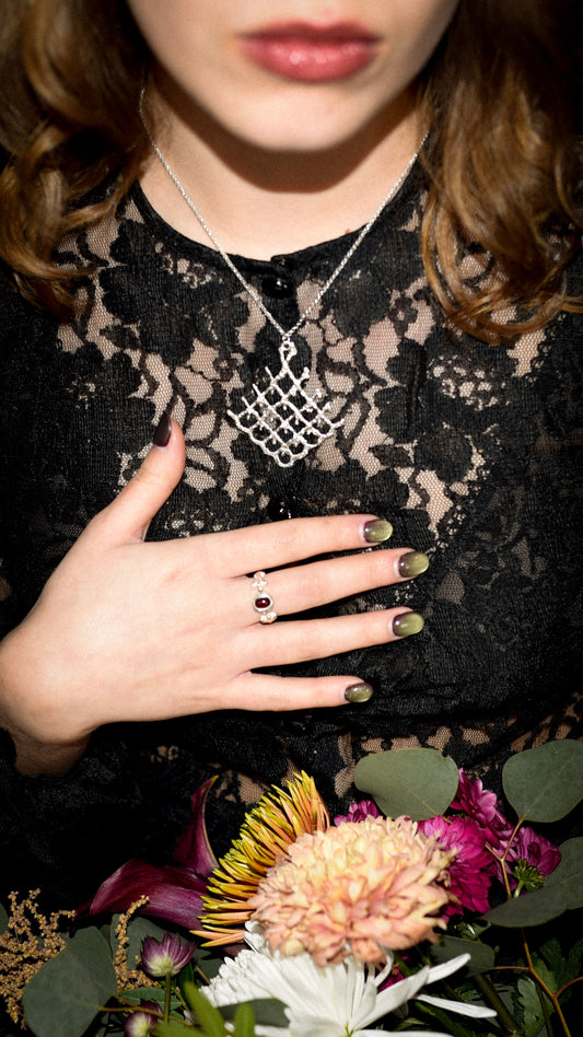 Person wearing a black lace top with a necklace, holding flowers on a dark background