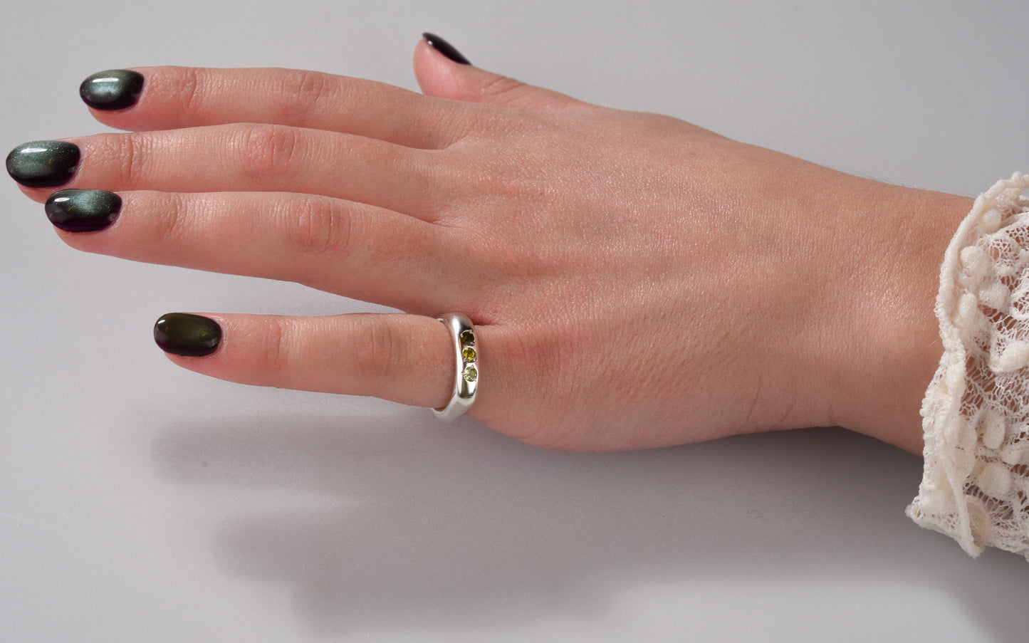 Hand with black nail polish and a ring on a neutral background