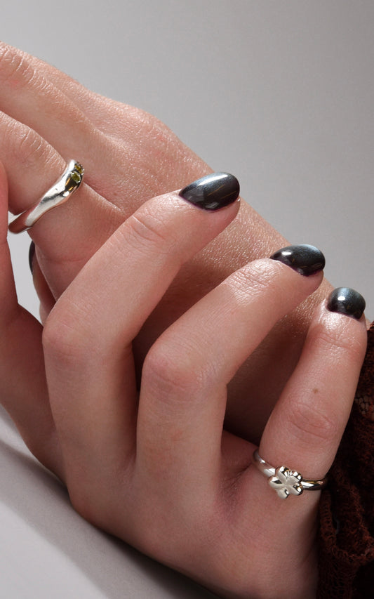 Close-up of a hand with black nail polish wearing two silver rings on a neutral background