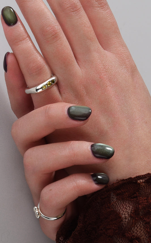 Close-up of a hand with dark nail polish and silver rings on a neutral background