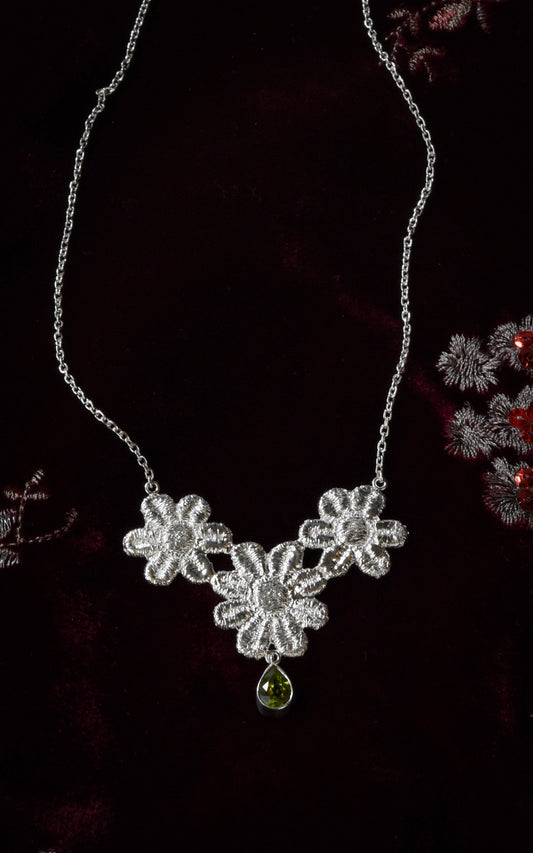 Silver floral lace necklace with a green gemstone on a dark red velvet background