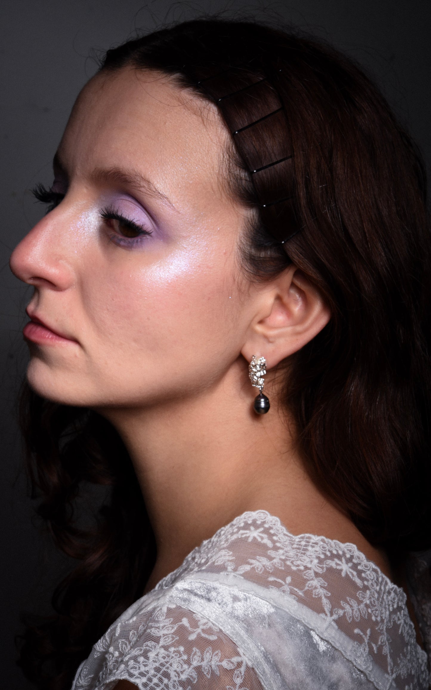 Close-up of a woman wearing a silver earring with black pearl with a dark background