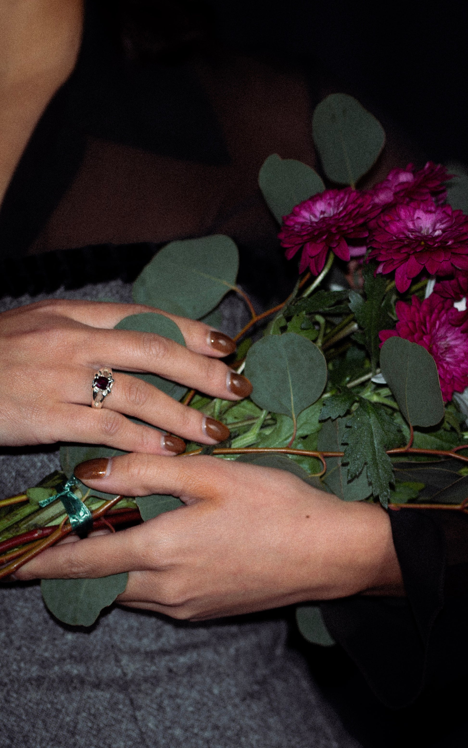 Close-up of hands wearing a silver ring holding a bouquet with a dark background