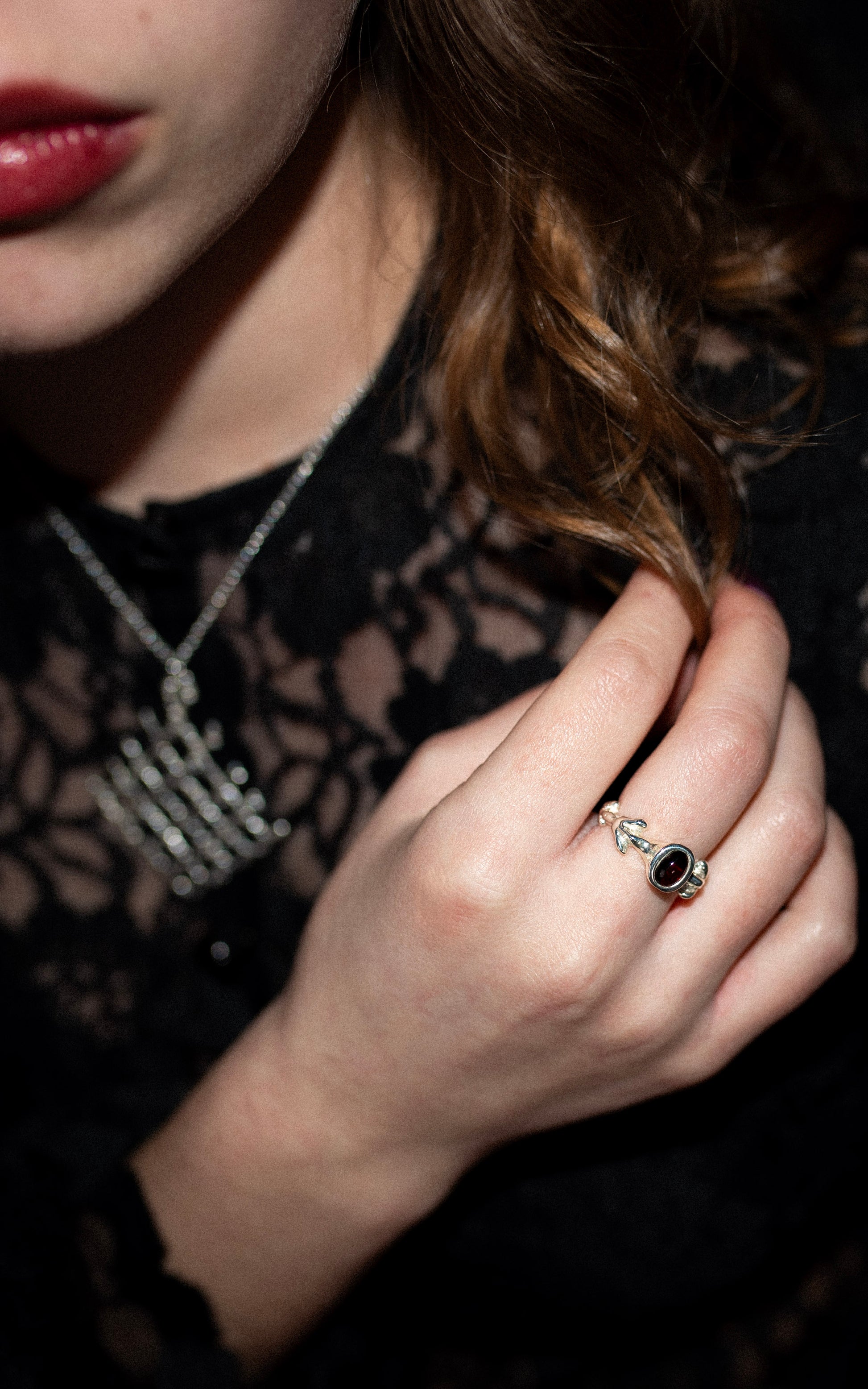 Close-up of a hand wearing a ring with a dark red oval gemstone, against a dark background.