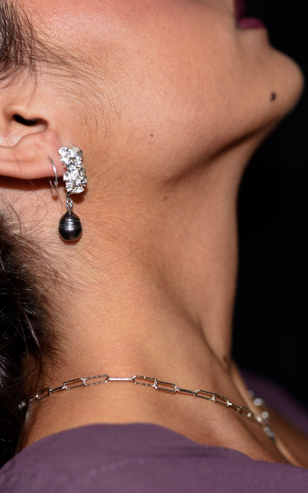 Close-up of a silver earring with a dark pendant on a blurred background