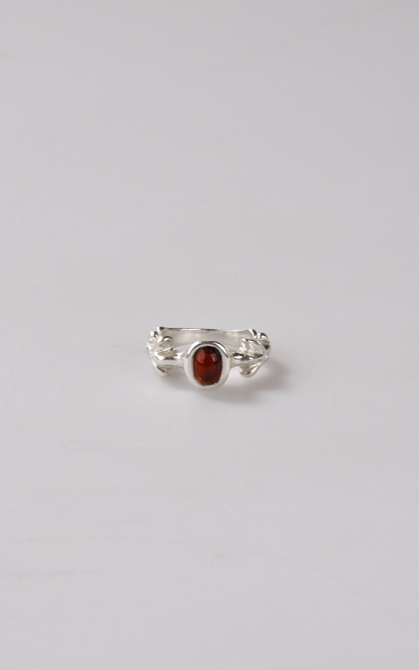 Silver ring with a red oval stone on a light gray background