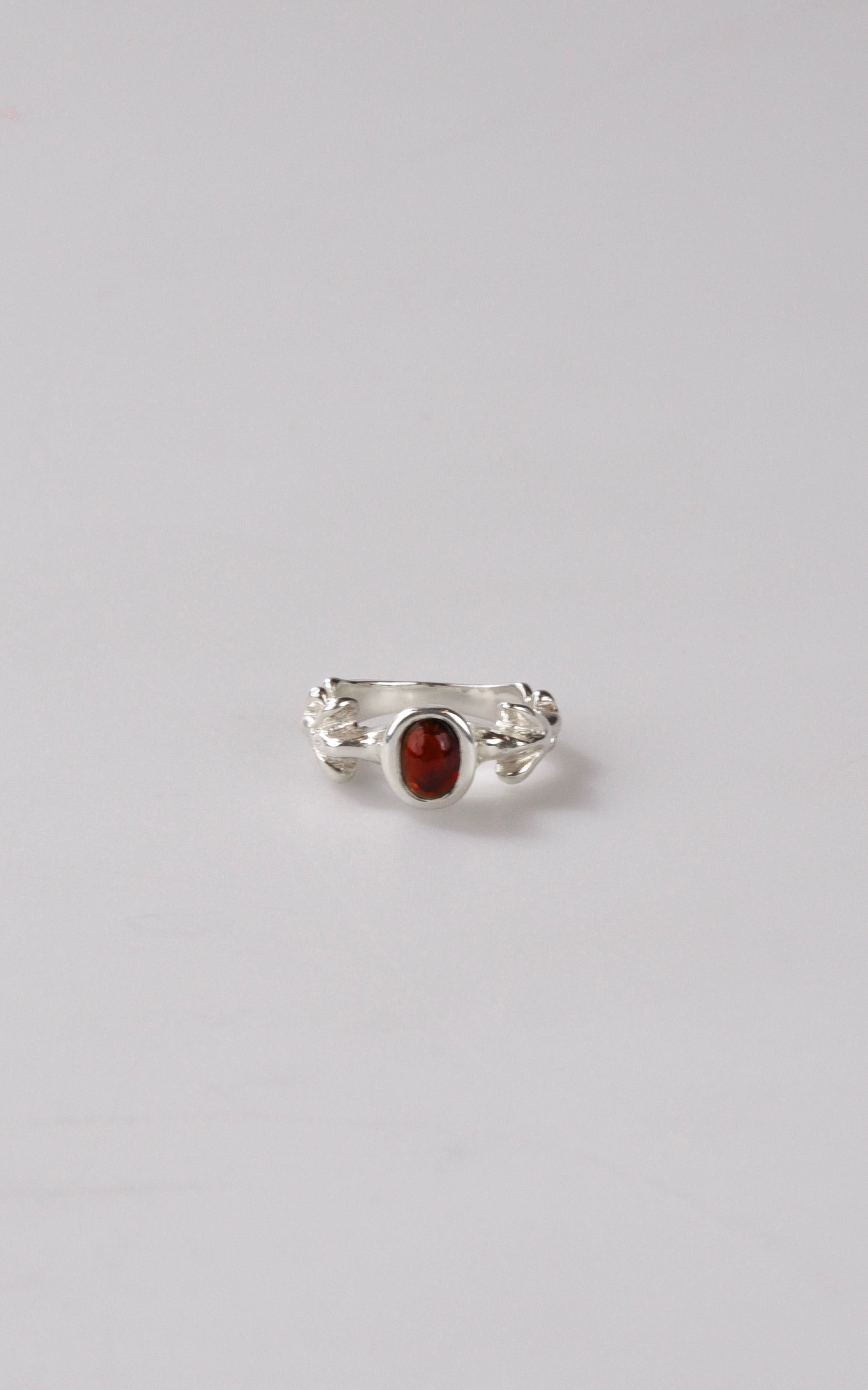 Silver ring with a red oval stone on a light gray background