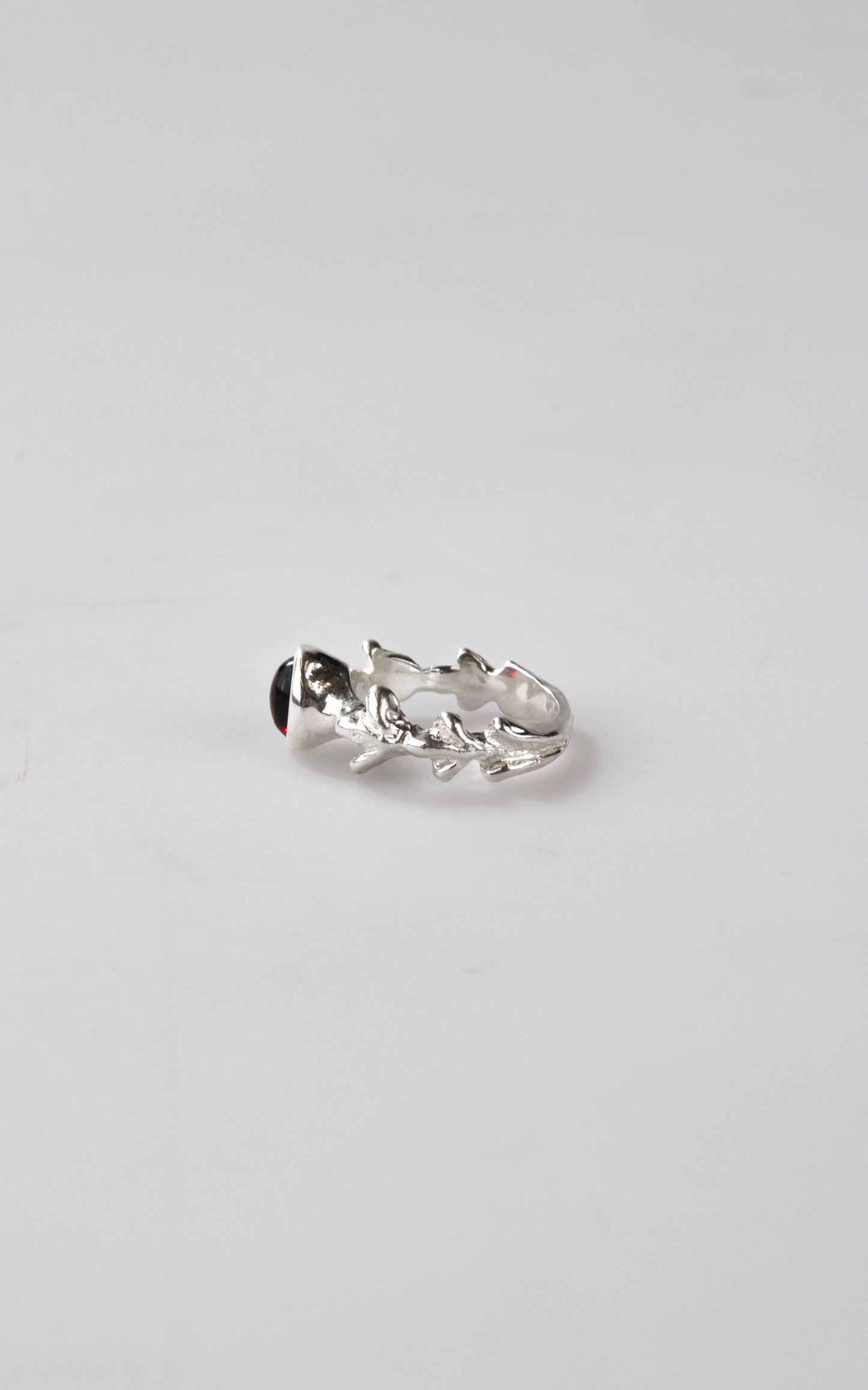 Silver ring with dark red gemstone on a light gray background
