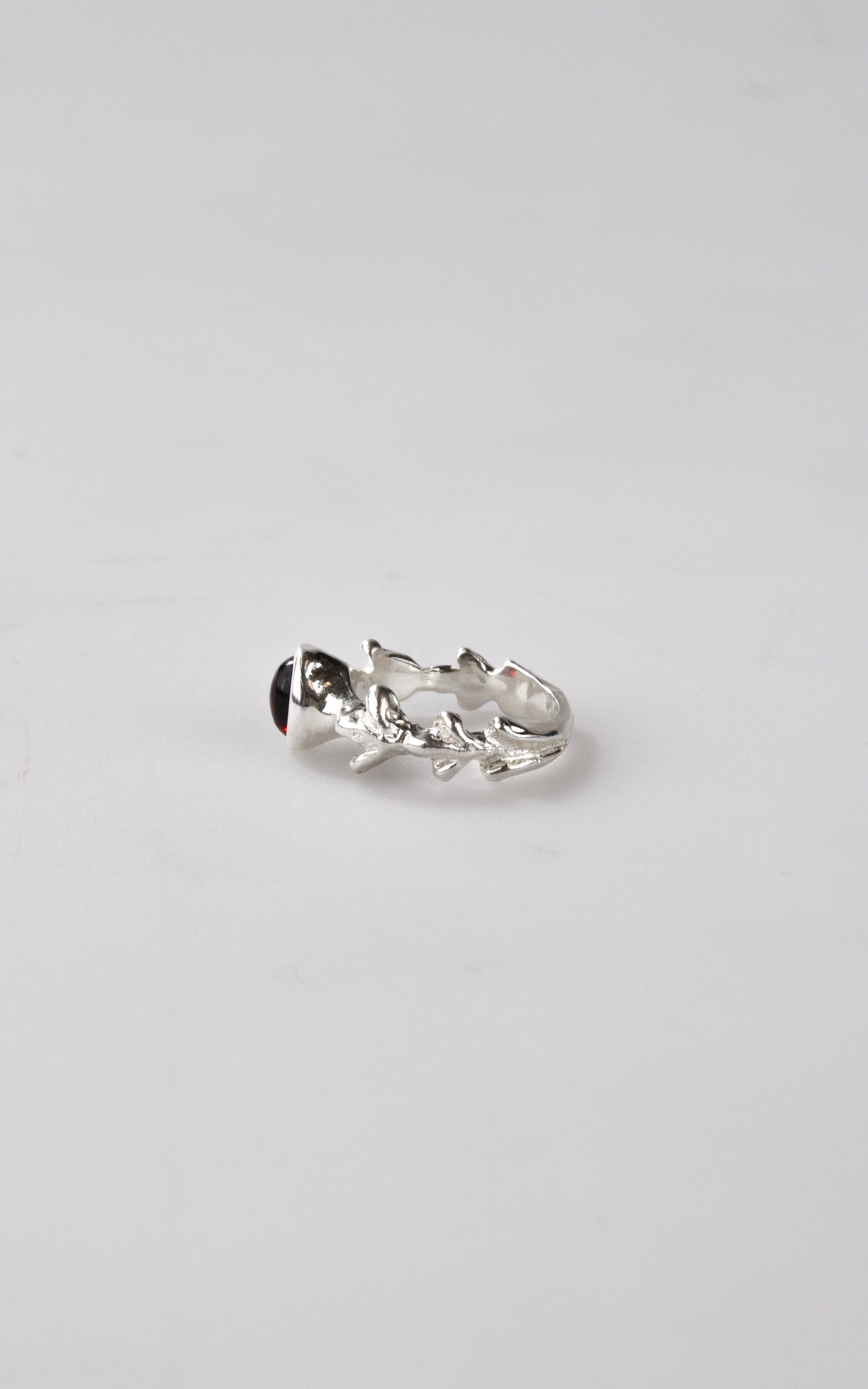 Silver ring with dark red gemstone on a light gray background