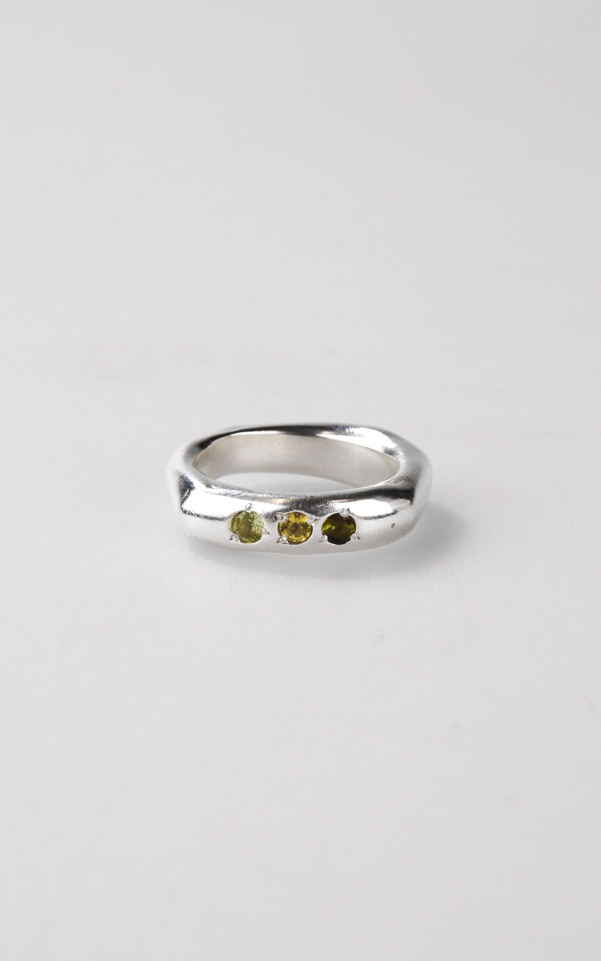 Handmade silver ring with three small tourmaline stones on a light gray background