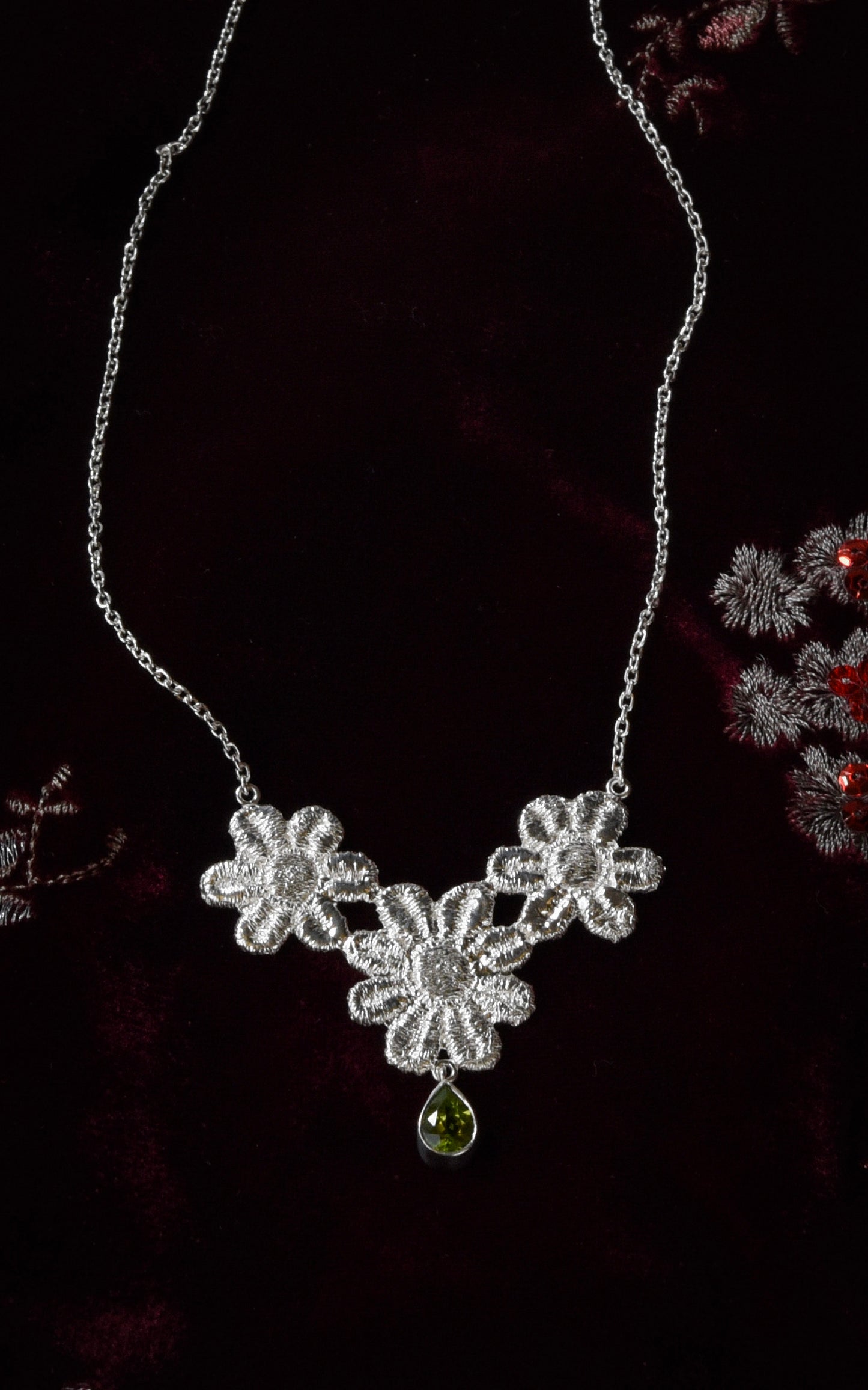 Silver floral lace necklace with a green gemstone on a dark red velvet background