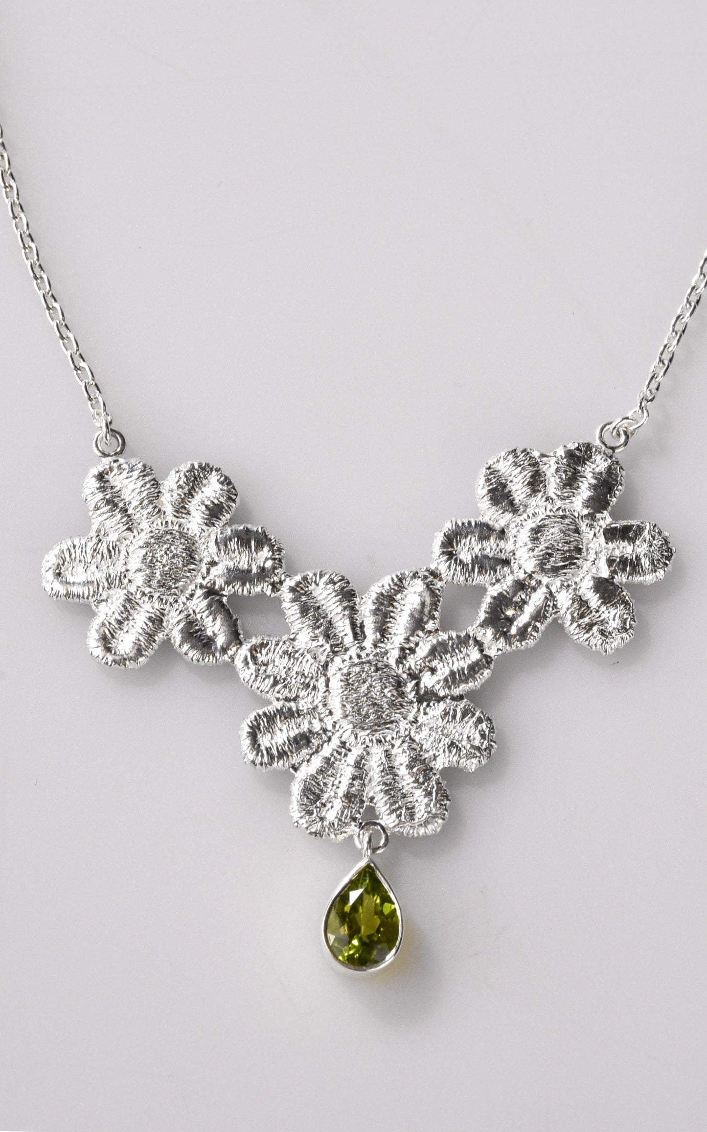 Silver floral lace necklace with a green gemstone on a light gray background