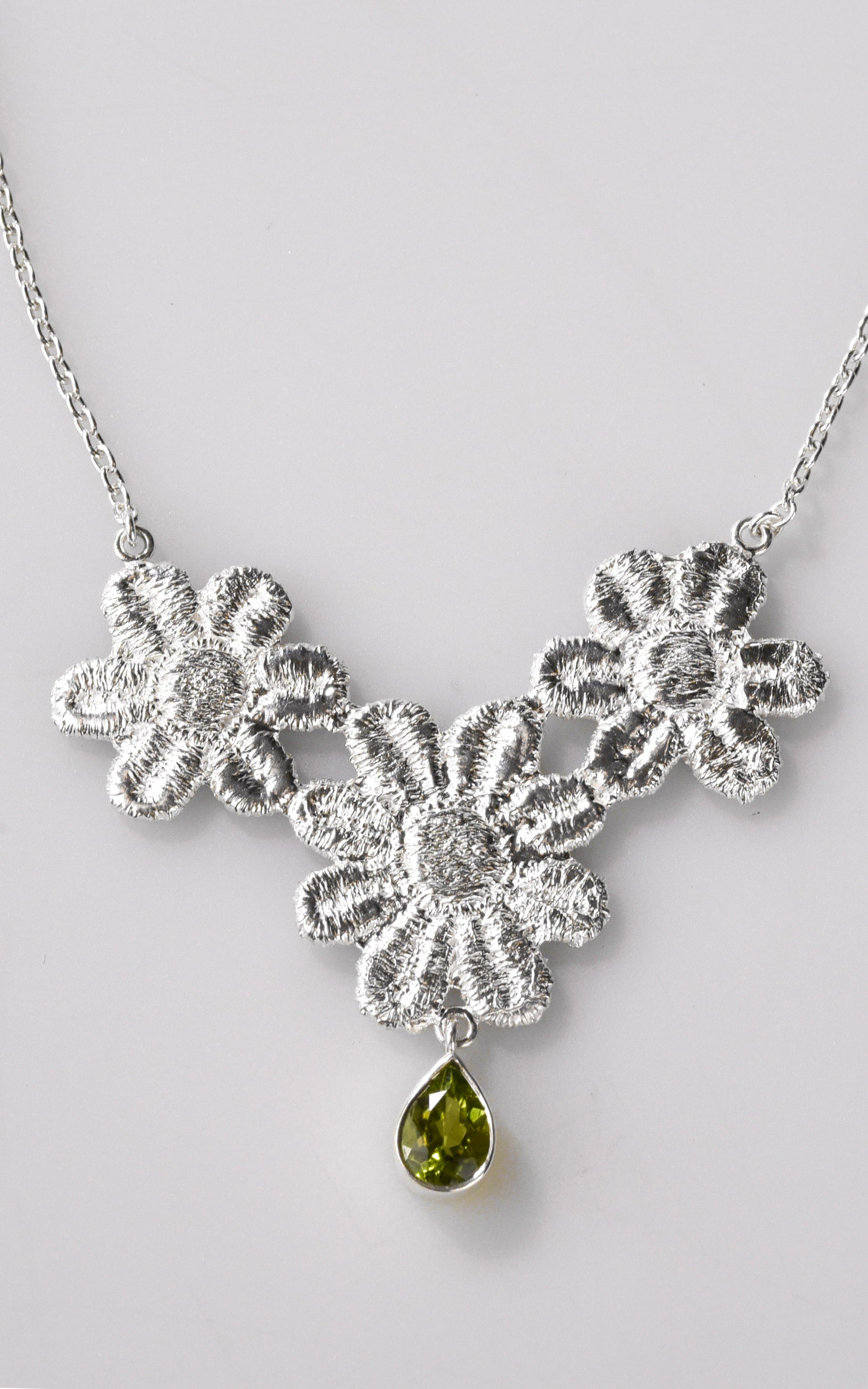 Silver floral lace necklace with a green gemstone on a light gray background