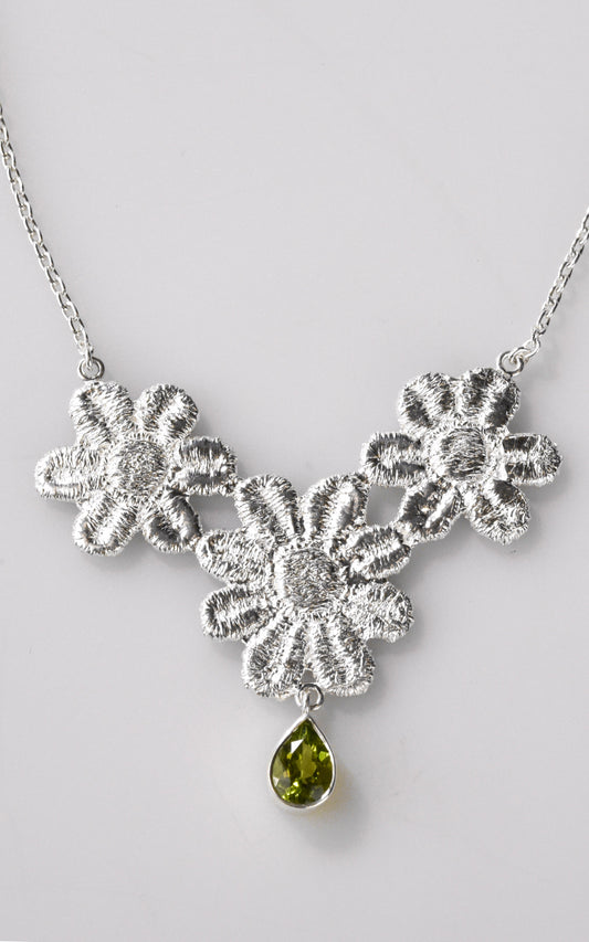 Silver floral lace necklace with a green gemstone on a light gray background
