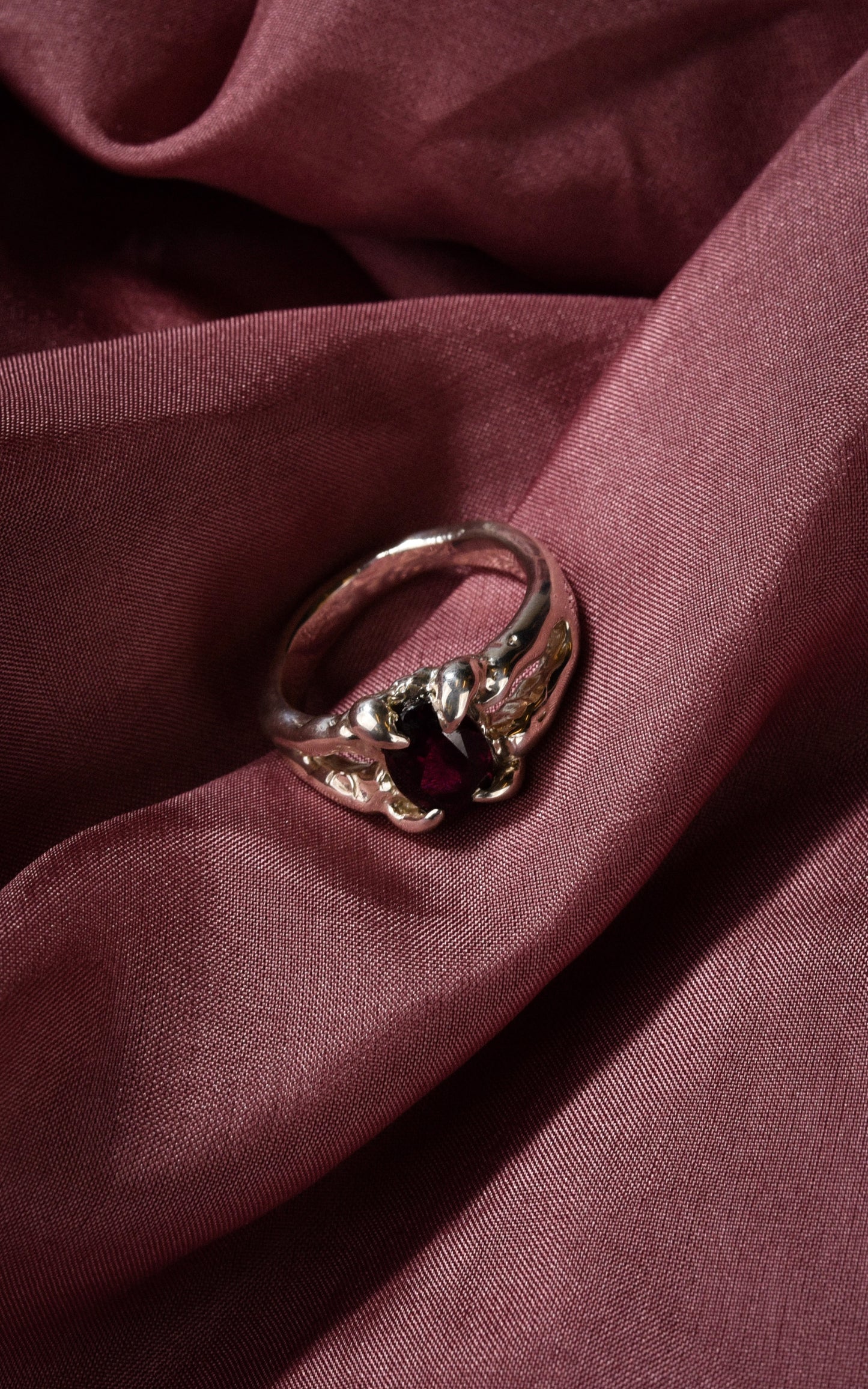 Silver ring with a burgundy maroon gemstone on a maroon fabric background