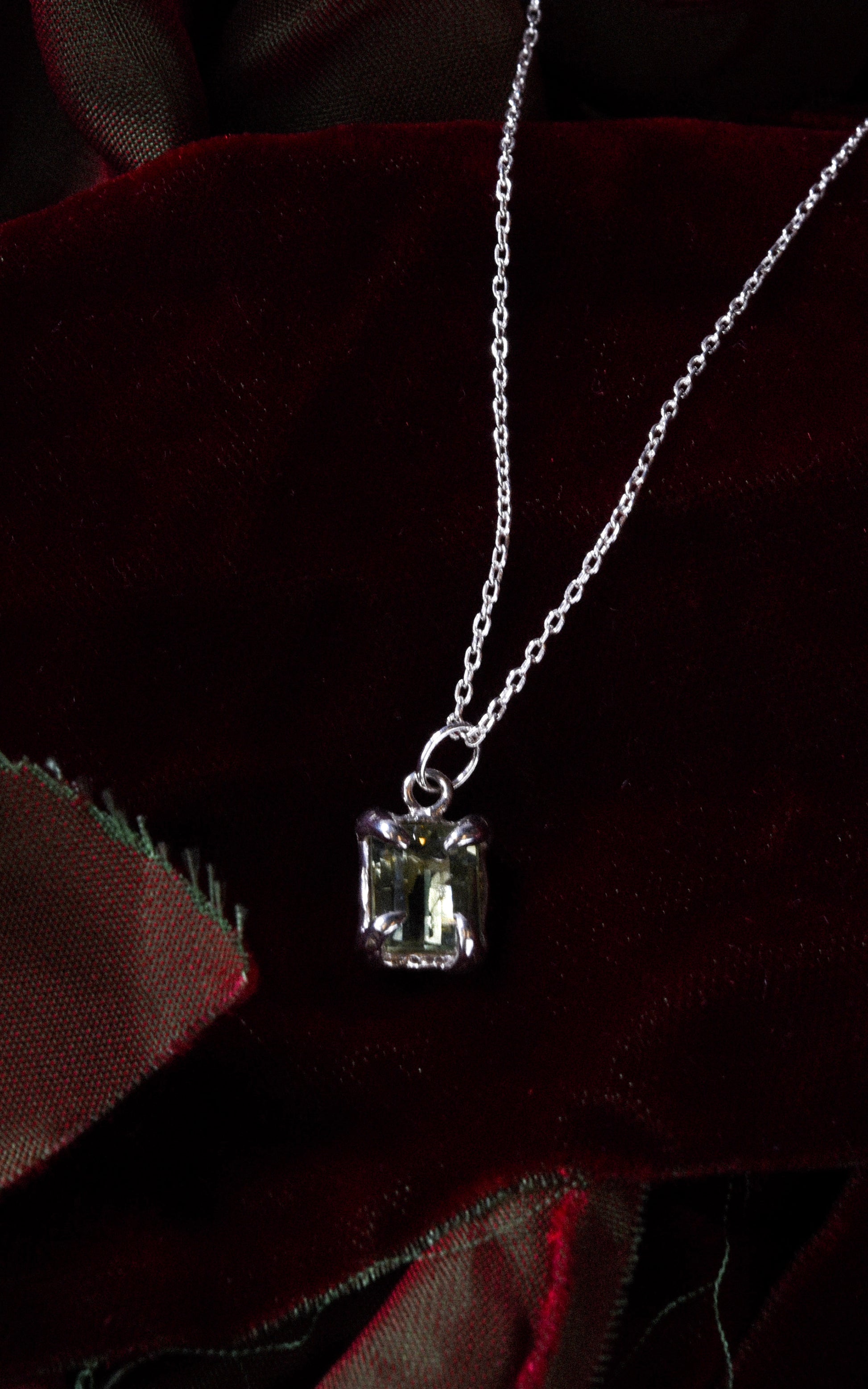 Silver necklace with a green gemstone pendant on a dark red velvet fabric background
