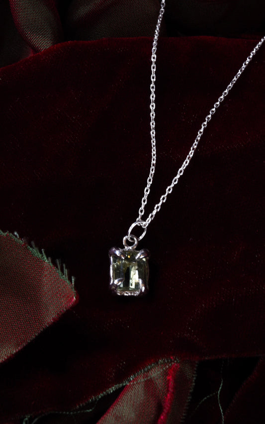 Silver necklace with a green gemstone pendant on a dark red velvet fabric background