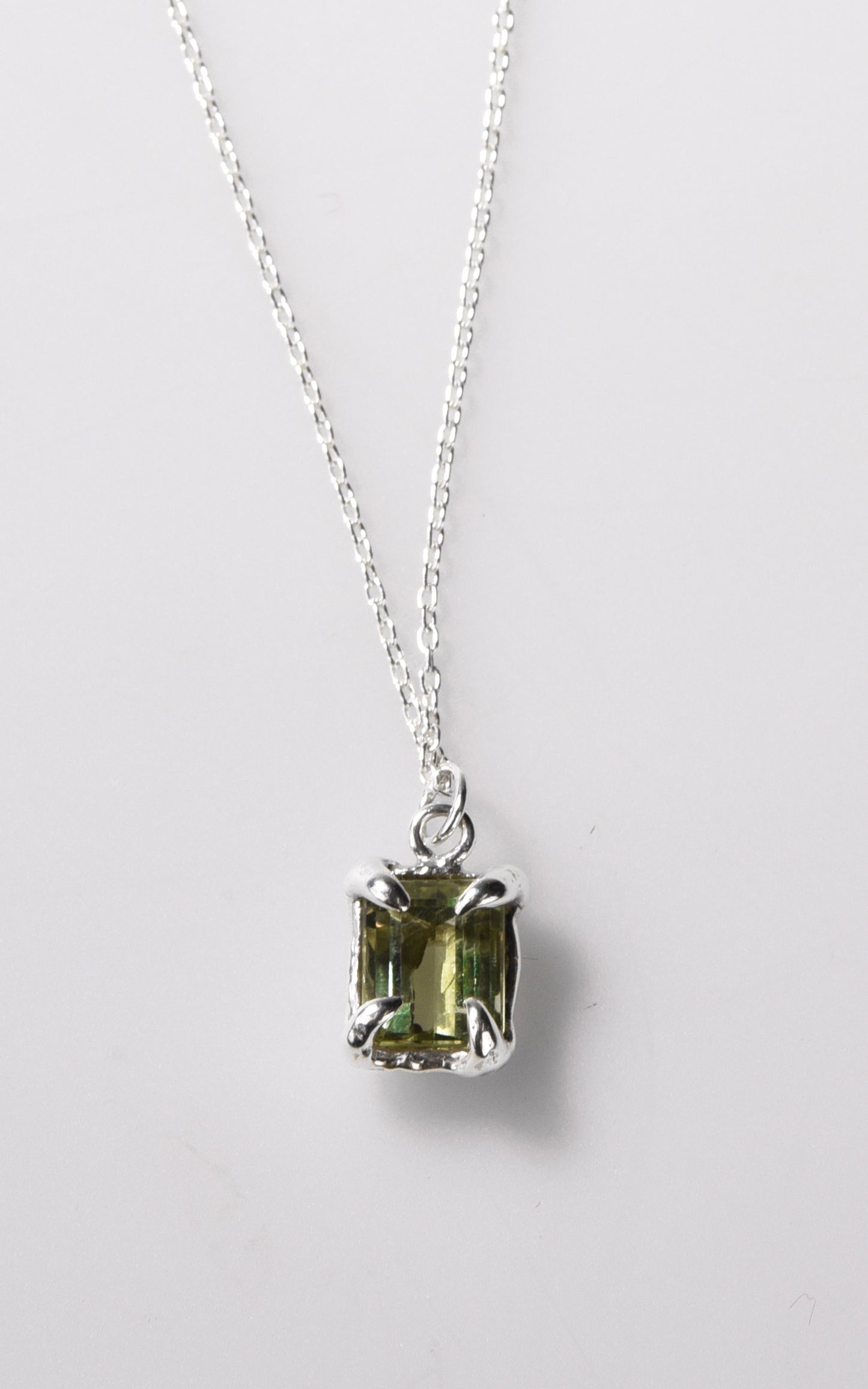 Silver necklace with a green gemstone pendant on a light gray background