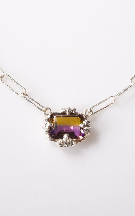 Silver necklace with a purple and yellow gemstone set in a silver pendant on a white background