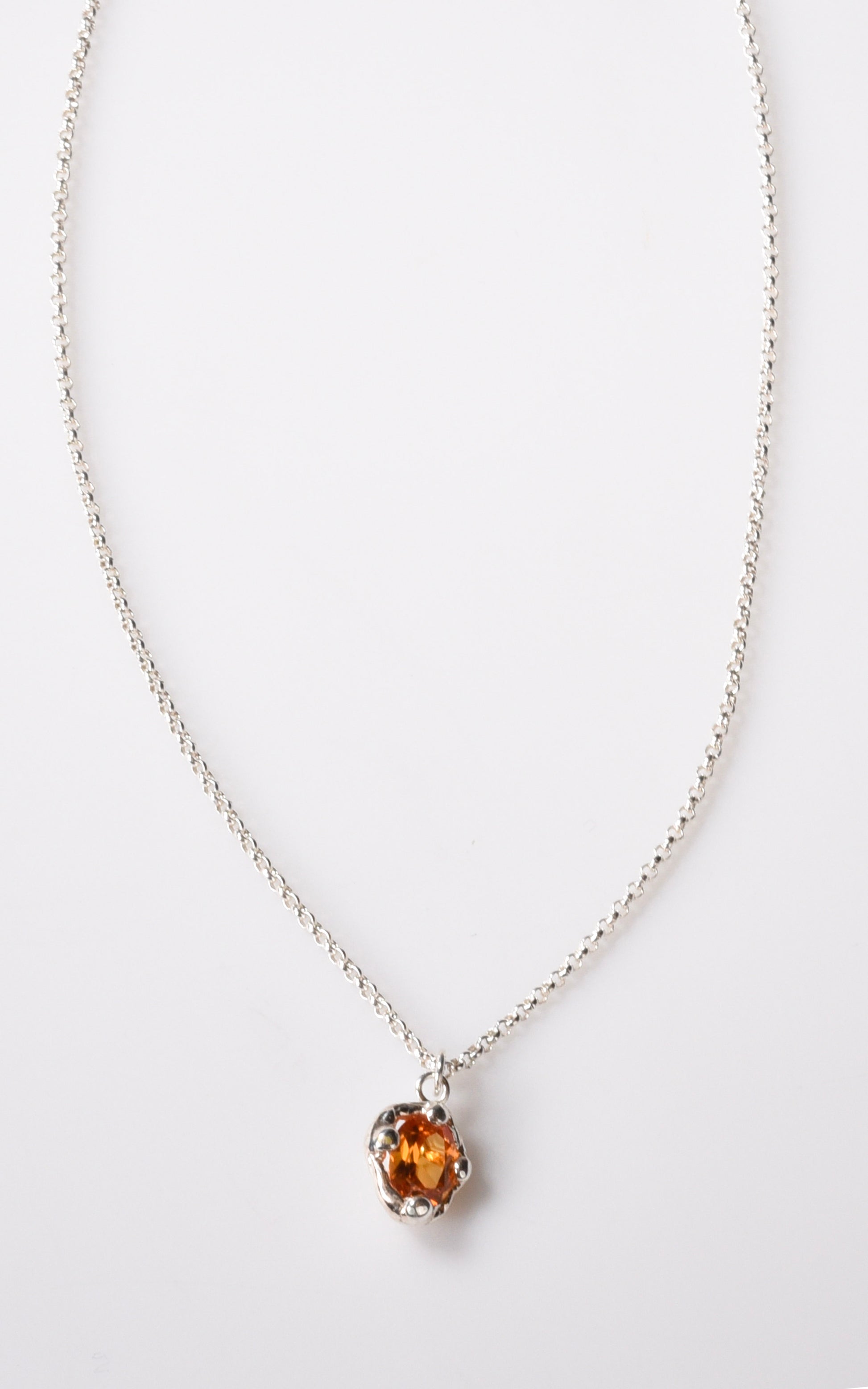 Silver necklace with an orange gemstone pendant on a white background