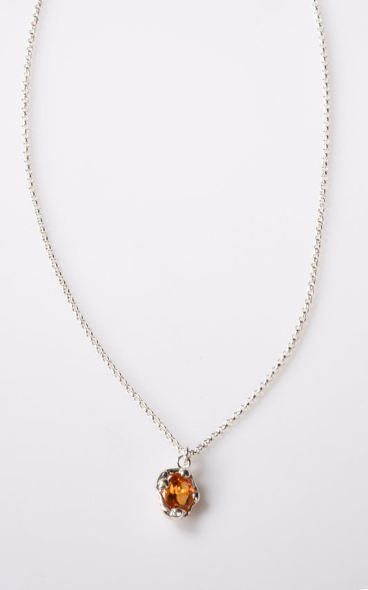 Silver necklace with an orange gemstone pendant on a white background