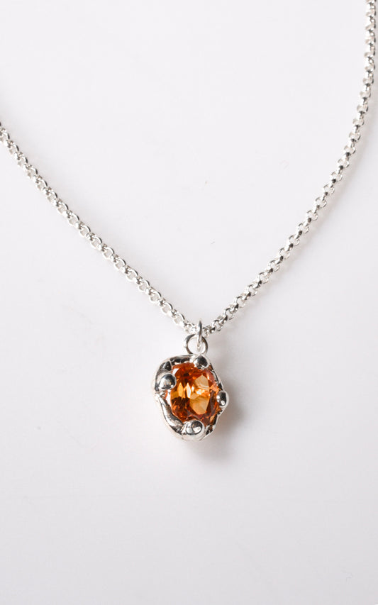 Silver necklace with an orange gesmtone pendant on a white background